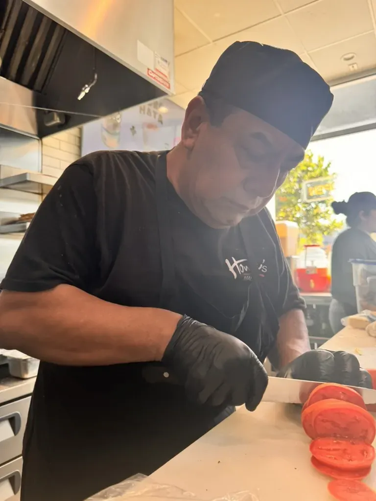 A cook slicing tomatoes on the line, afternoon light from the windows behind him.